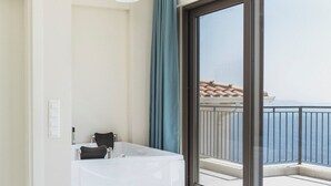 Een moderne hotelkamer met een groot bed, een badkuip, en een balkon met uitzicht op zee.