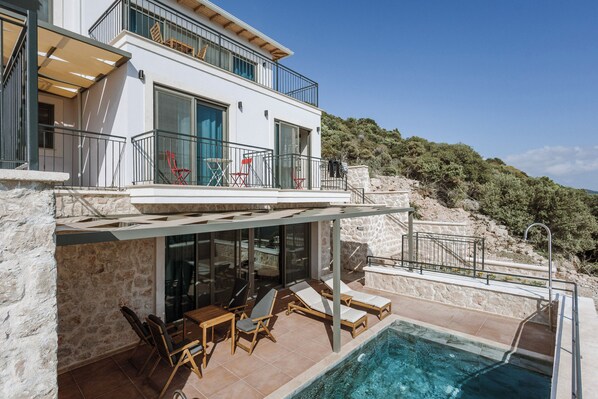 A modern two-story house with a swimming pool, outdoor seating, and a stone wall.