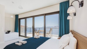 Een hotelkamer met een groot bed, een balkon met uitzicht, een badkuip en een tafel met stoelen.