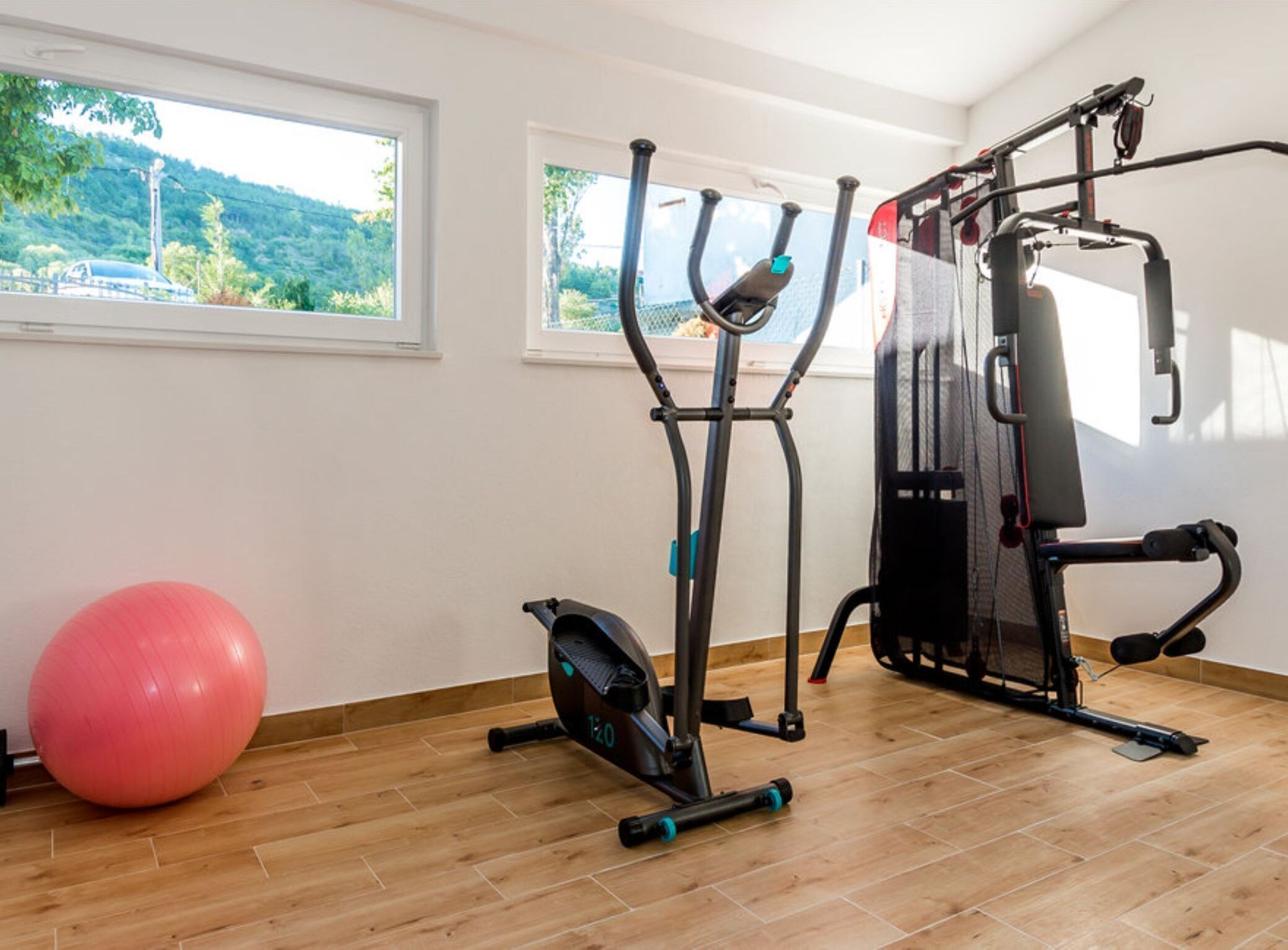 Une salle de sport équipée de matériel d’exercice, d’un grand ballon de gymnastique et d’une fenêtre donnant sur un espace verdoyant.