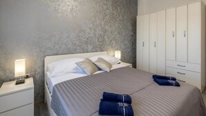 A neatly made bed with pillows, a bedside lamp, and a wardrobe with multiple doors. - Perla Charming Apartment No1 (Kastela)