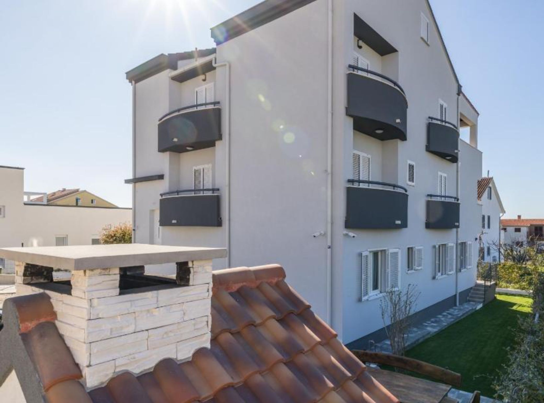 Un immeuble résidentiel moderne à plusieurs étages, doté de balcons, d’un toit plat et d’une pelouse bien entretenue.