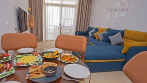 A dining area with a glass table, chairs, and a variety of dishes. A blue sofa with yellow cushions is in the background. - Spacious Two bedroom in Azzurra with Terrace Sahl Hasheesh (Sahl)