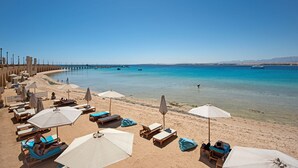 A beach with sun loungers and umbrellas, a pier in the background, and clear blue water. - Spacious Two bedroom in Azzurra with Terrace Sahl Hasheesh (Sahl)