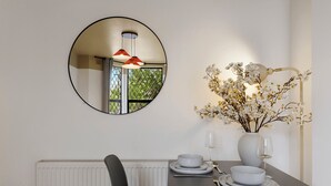 Un'area pranzo con uno specchio rotondo, un vaso con fiori bianchi e un tavolo apparecchiato con piatti, ciotole e posate.
