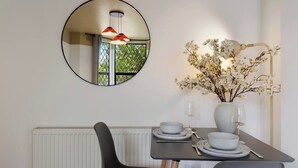 A dining area with a round mirror, a vase with flowers, and a table set for two. - Evershot Rd N4, Crouch Hill, Finsbury Park (London)
