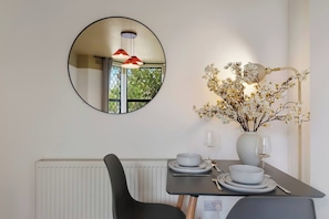 A dining area with a round mirror, a vase with flowers, and a table set for two.