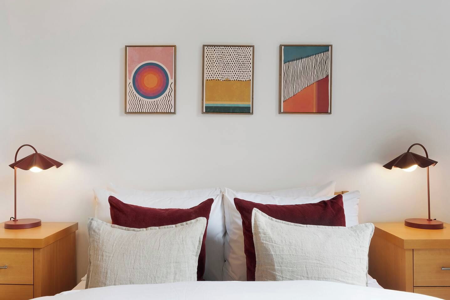 A bed with white and red bedding, two bedside lamps, and three framed artworks on the wall.