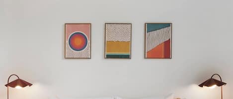 A bed with white and red bedding, two bedside lamps, and three framed artworks on the wall.