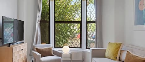 A living room with a sofa, armchair, TV, and a large window with a view of greenery.