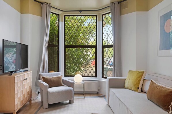 A living room with a sofa, armchair, TV, and a large window with a view of greenery.