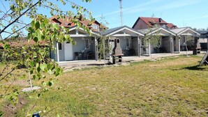 A row of small, single-story houses with numbered doors, a barbecue grill, and a clear sky.