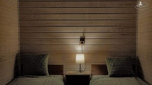 A cozy room with wooden panel walls, two beds with matching pillows, and a bedside table with a lamp.