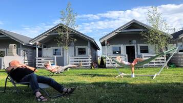 A grassy area with two cabins, each with a porch and a door.