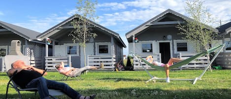 A grassy area with two cabins, each with a porch and a door.