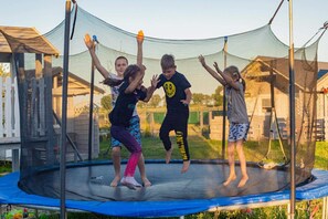 Un trampoline doté d’un filet de sécurité, entouré d’une clôture en bois, avec des maisons en arrière-plan.