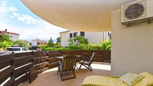 A patio with a table and chairs, a sunshade, a lounge chair, and a wall-mounted air conditioning unit.