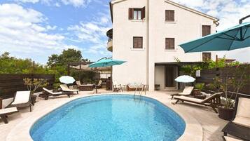 A swimming pool with lounge chairs and umbrellas, surrounded by a building with balconies.
