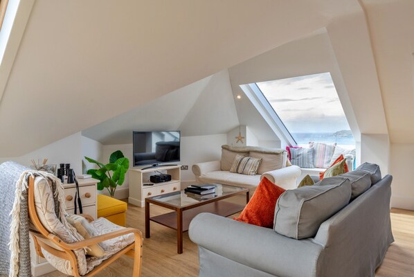A modern loft apartment with a large skylight, a cozy seating area with a sofa and armchair, a flat-screen TV, and a small side table. - Apartment in Woolacombe Near Award-winning Beach (Woolacombe)