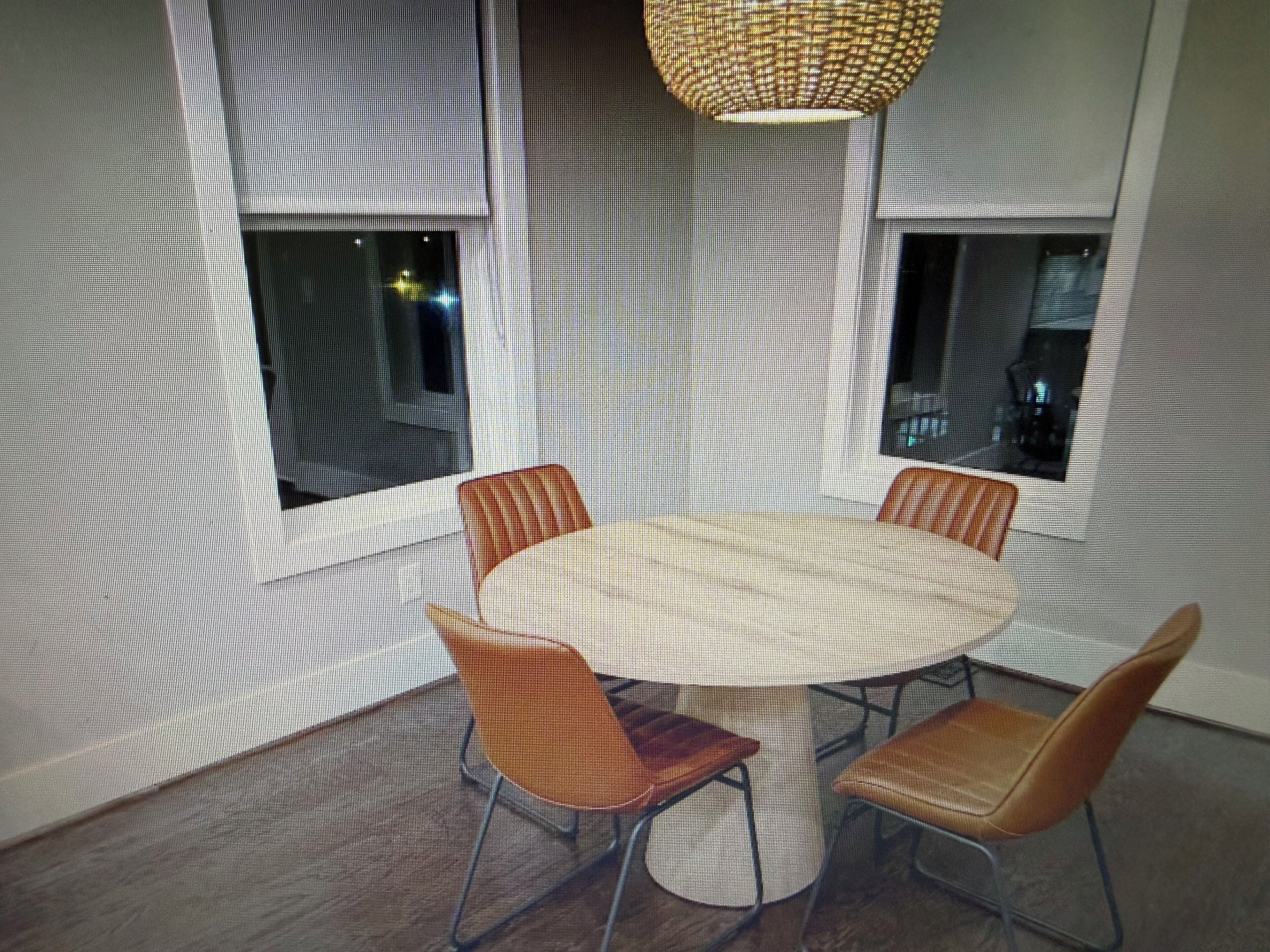 A conference room with a round table and four chairs, large windows, and a woven light fixture.