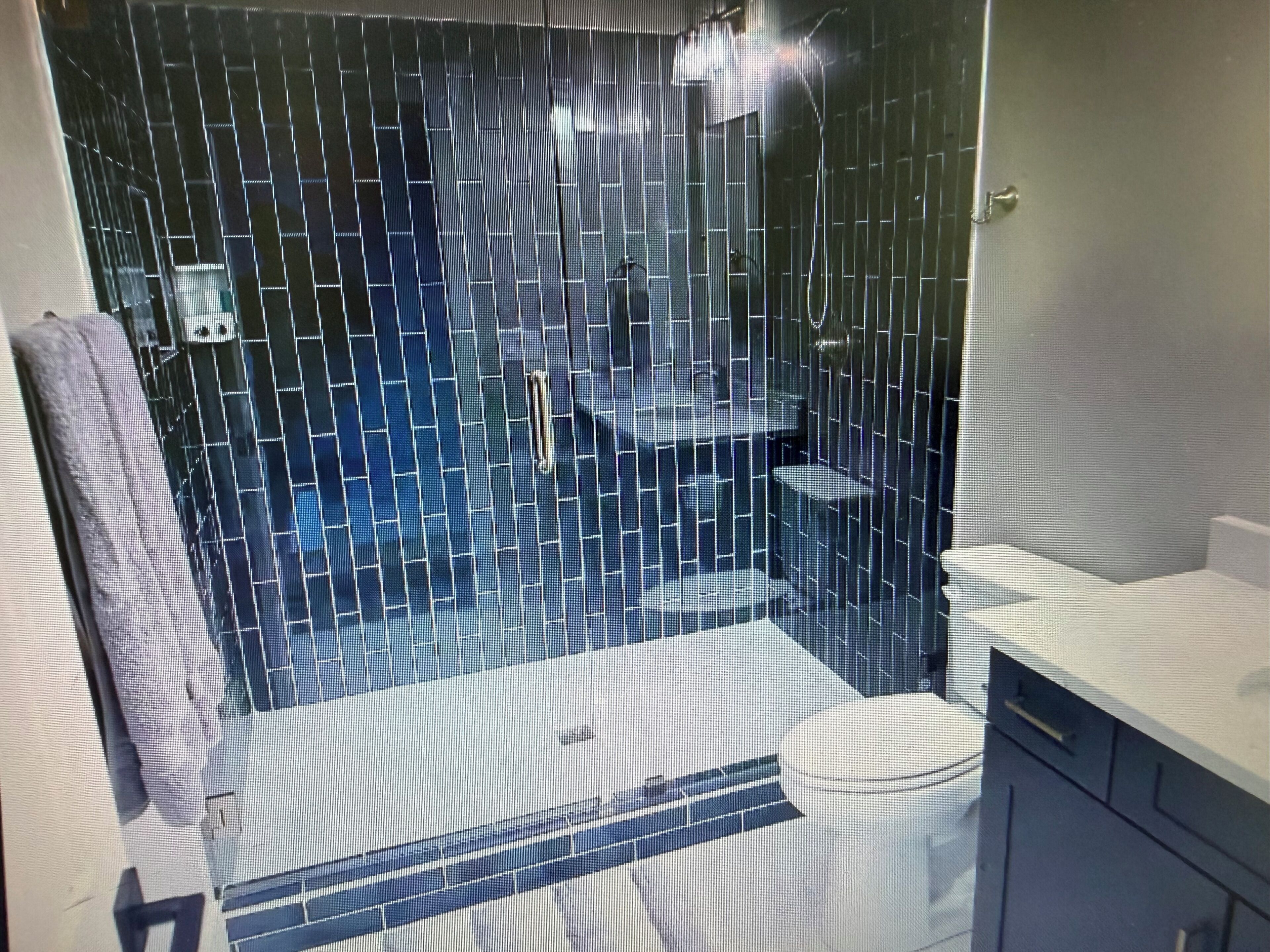 A bathroom with a tiled shower enclosure, a toilet, and a sink area.