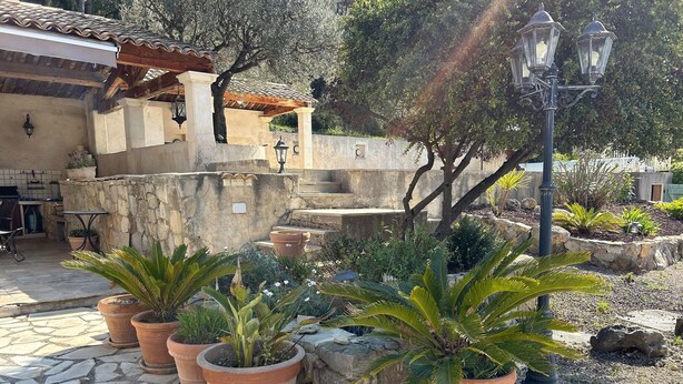 A courtyard with stone flooring, potted plants, a pergola, and a street lamp.