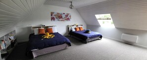 A bedroom with two beds, a ceiling fan, a window, and a painting on the wall.