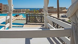 A balcony with a pool, palm trees, and a clear view of the sea.