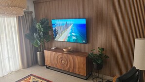 Un salon moderne avec un téléviseur à écran plat, un meuble en bois, des plantes en pot et un tapis à motifs.