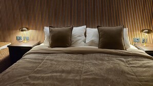 Un lit bien fait, recouvert d’une couverture marron, avec deux oreillers blancs et deux oreillers marron. De chaque côté du lit, on trouve une table de chevet sur laquelle est posée une lampe.