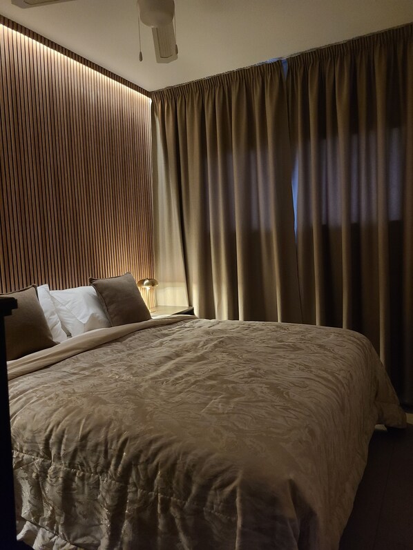 A hotel room with a large bed, a bedside table with a lamp, and a view of the outside through curtains.