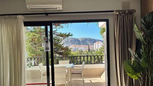 Un balcon doté de meubles en osier, offrant une vue sur les bâtiments et les montagnes, et équipé d’un climatiseur.