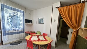 A room with a round table, red chairs, a TV on the wall, and a patterned curtain. - Appartamento Casa Delle Rose (San Michele al Tagliamento)