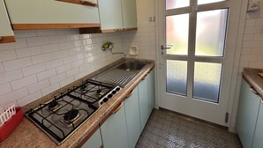 A kitchen with a gas stove, a sink, and light blue cabinets. - Appartamento Casa Delle Rose (San Michele al Tagliamento)