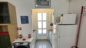 A compact kitchen with a washing machine, a microwave, and a refrigerator. There's a fire extinguisher mounted on the wall. - Appartamento Casa Delle Rose (San Michele al Tagliamento)