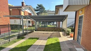 A covered patio area with a brick wall, a metal fence, and a paved walkway. - Appartamento Casa Delle Rose (San Michele al Tagliamento)