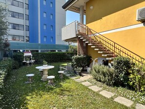 Un patio con un pequeño jardín, una escalera y un edificio con fachada azul y amarilla.