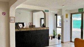 A reception area with a glass table, two cushioned chairs, a black counter, and a green exit sign. - Calma Chicha Rooms (Playa del Carmen)