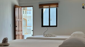 A bedroom with two beds, a wooden door, a window with blinds, and a swan-shaped towel on one bed. - Calma Chicha Rooms (Playa del Carmen)