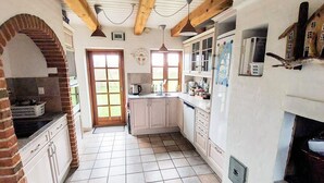 Una cocina con suelo de baldosas, vigas de madera, un arco de ladrillo y una ventana con vistas al exterior.