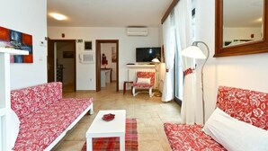 A living room with a sofa, a small table, a TV, and a lamp. - Charming Apartment With Balcony and Pool (Vodnjan)