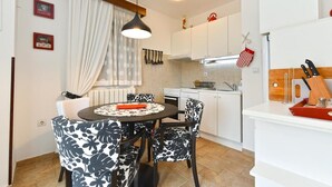 A compact kitchen with white cabinets, a dining table with patterned chairs, and a hanging light fixture. - Charming Apartment With Balcony and Pool (Vodnjan)