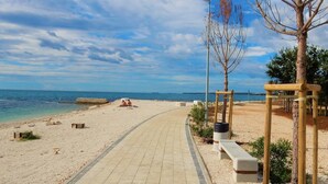 A paved walkway along a beach with a wooden structure and benches. - Charming Apartment With Balcony and Pool (Vodnjan)