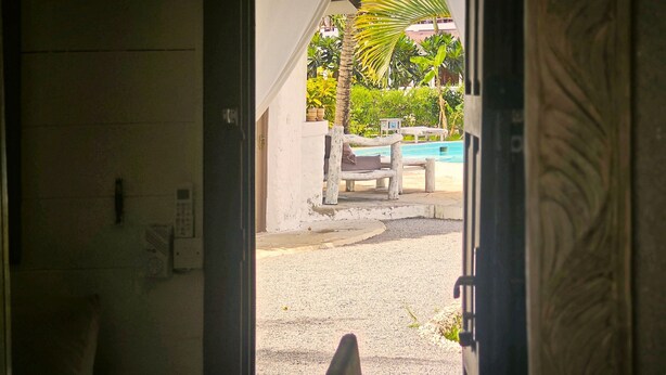 An open doorway leading to a pool area with a wooden deck, lounge chairs, and a palm tree. - Kisiwa Apartments Watamu at Ascot Resort  (Watamu)