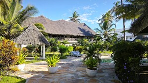 Un resort tropical con una estructura de techo de paja, una zona de piscina y abundante vegetación.