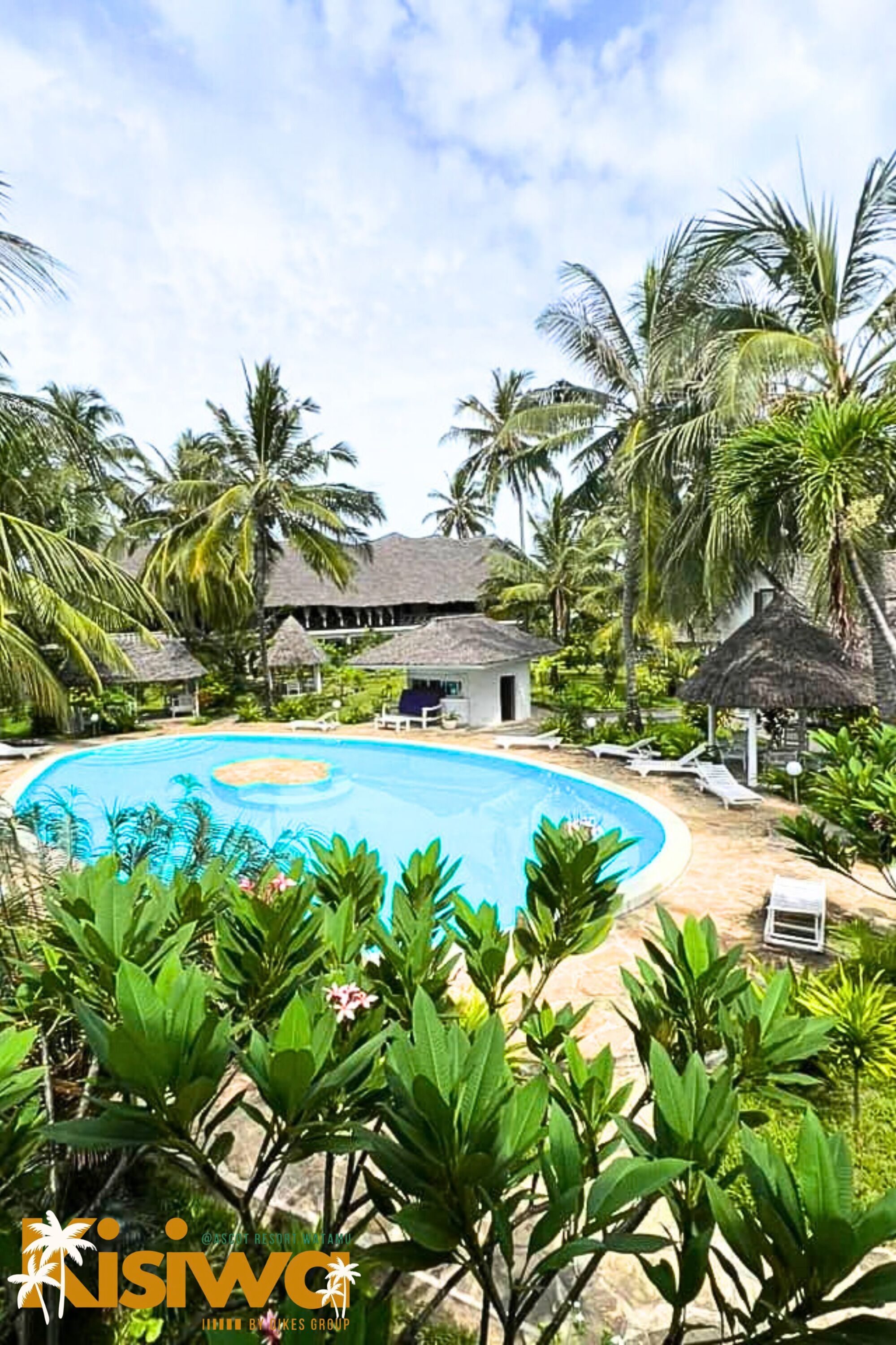Resort com piscina rodeada por vegetação exuberante e palmeiras. Possui estruturas com telhados de palha e cadeiras de descanso.