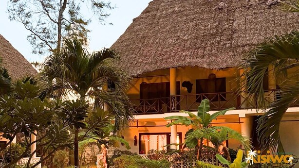 Un resort con edificios de techo de paja, palmeras y un jardín bien cuidado.
