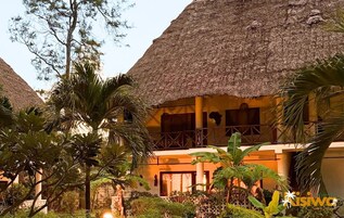 A resort with thatched-roof buildings, palm trees, and a well-maintained garden.