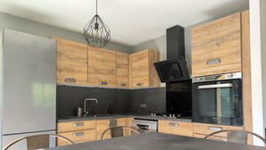 A modern kitchen with wooden cabinets, a black countertop, a stainless steel oven, and a hanging light fixture.