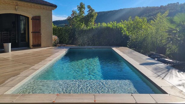 A rectangular swimming pool with clear water, surrounded by a wooden deck and a stone wall.